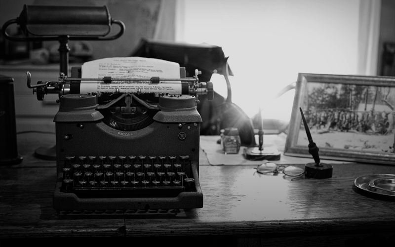 A vintage typewriter on a wooden desk beside a framed photograph and an inkwell.