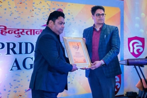 Rohit Jain holding a framed certificate in front of a Hindustan Pride of Agra backdrop.