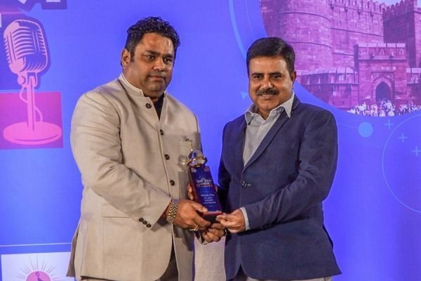 Rohit Jain accepting a trophy from another guest on a lit stage at a Zee News conclave.