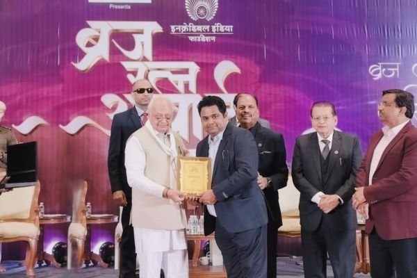 An elderly dignitary in white presenting the Braj Ratna Alankaran Samman certificate to Rohit Jain on stage.