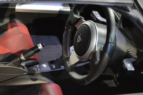 The carbon-fibre cockpit of a Tesla Roadster, with red seats and the Tesla badge on the steering wheel.