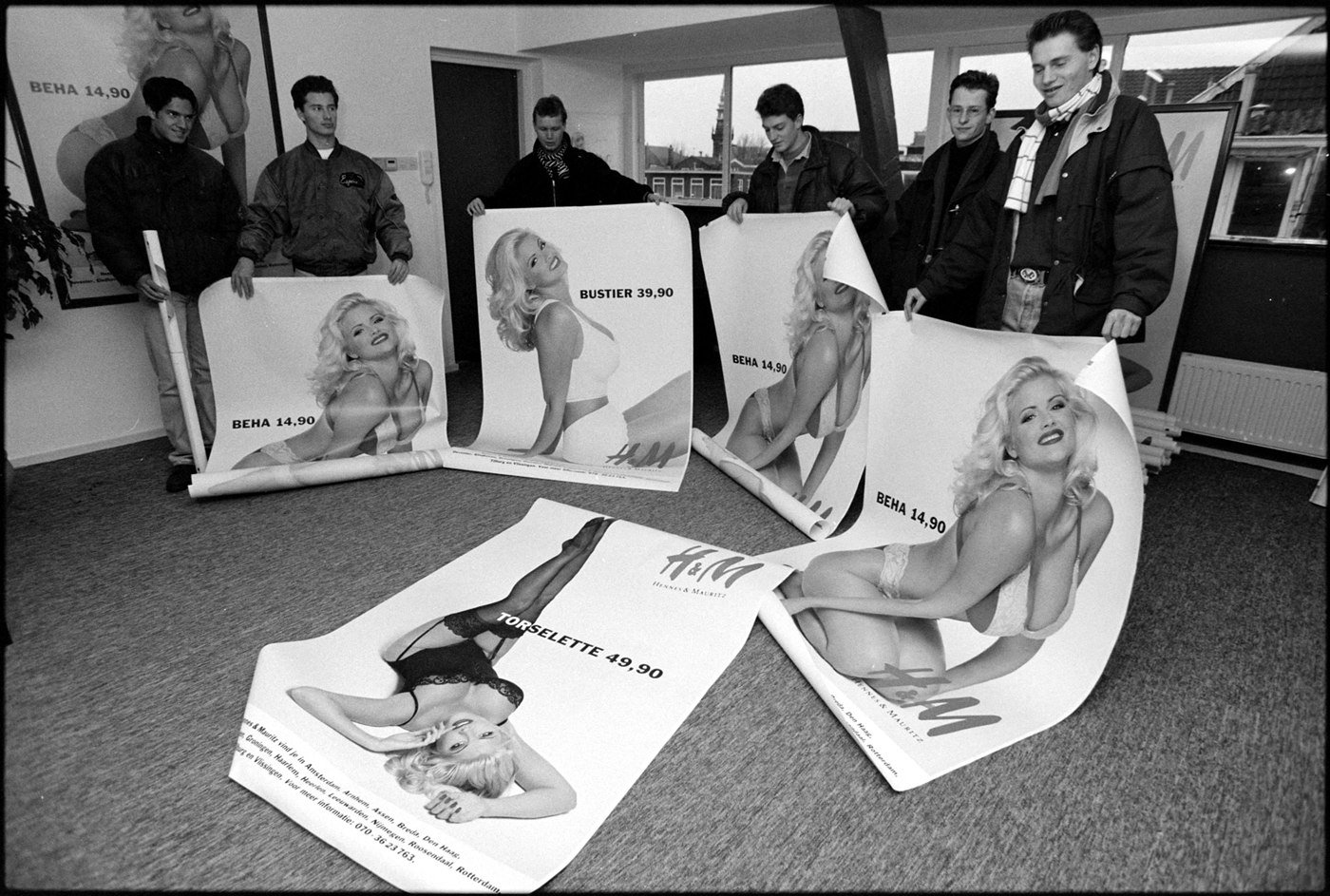 Young people in a room in the Netherlands holding and unrolling large H&M advertising posters of a blonde model, December 1993.