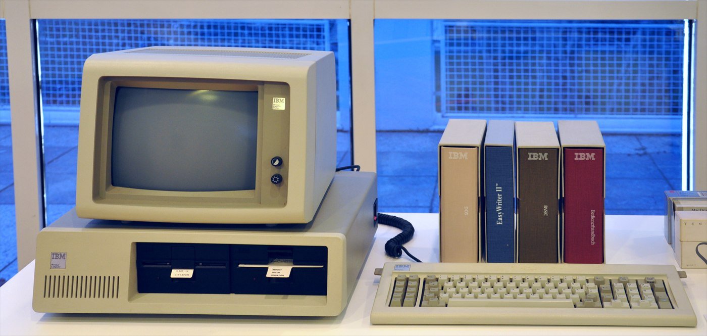 An IBM Personal Computer of 1981 with its monitor and keyboard, beside a row of original manuals, in a museum display.