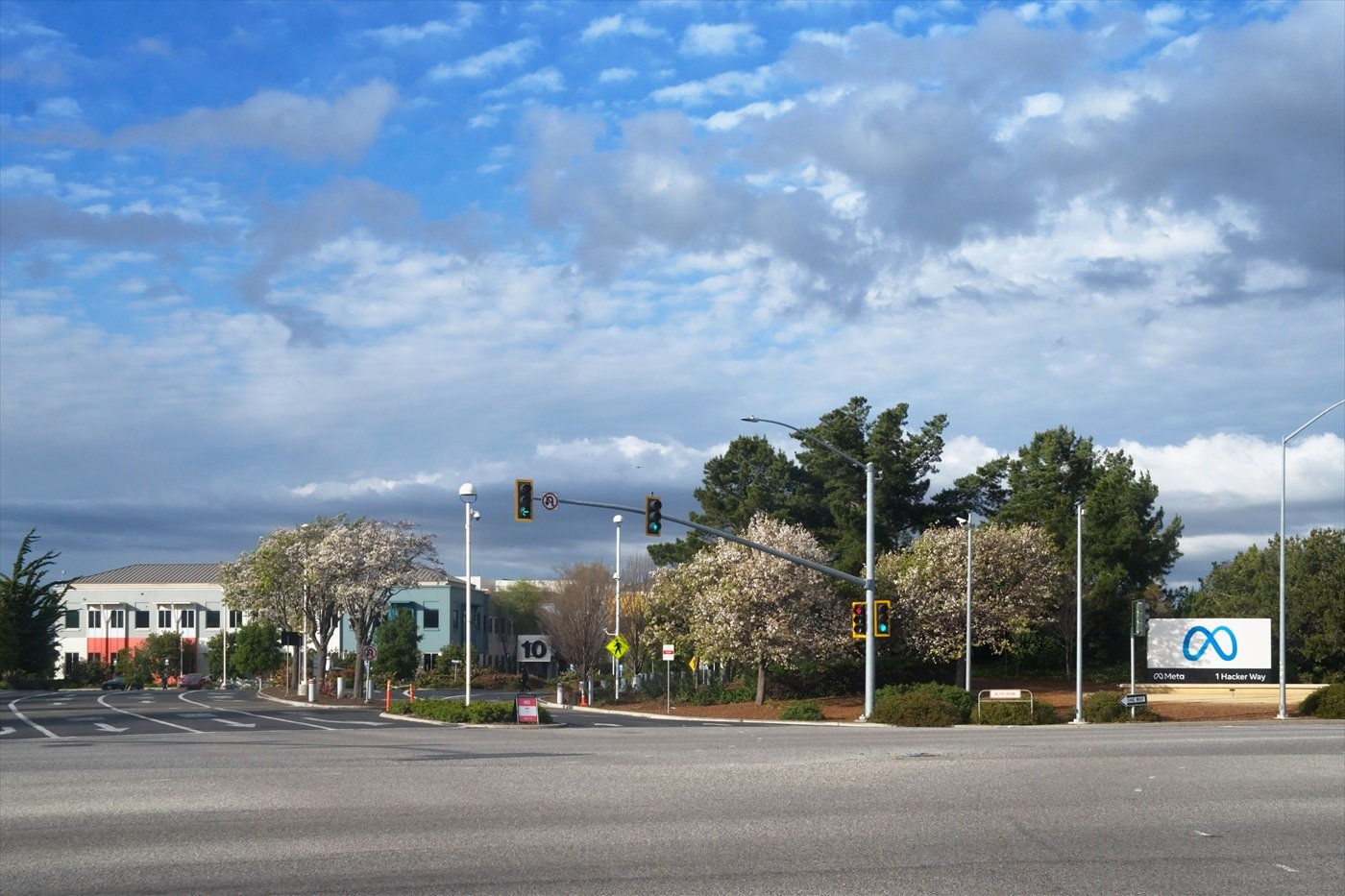 The entrance to Meta’s headquarters campus in Menlo Park, with the Meta sign beside the road beneath a cloudy sky.