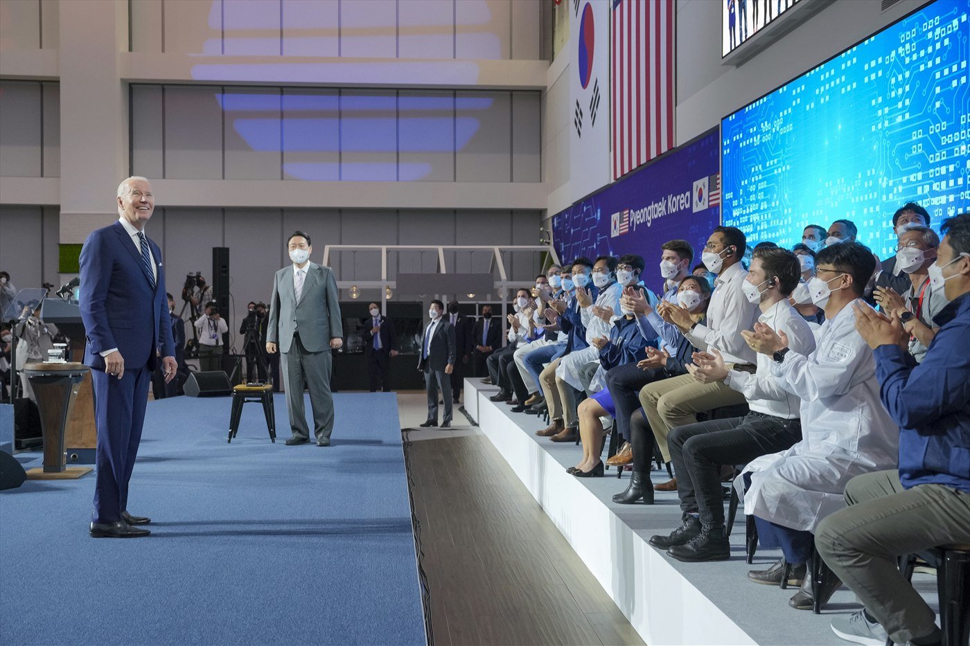 Joe Biden standing on a blue carpet addressing rows of seated Samsung employees beneath United States and South Korean flags.