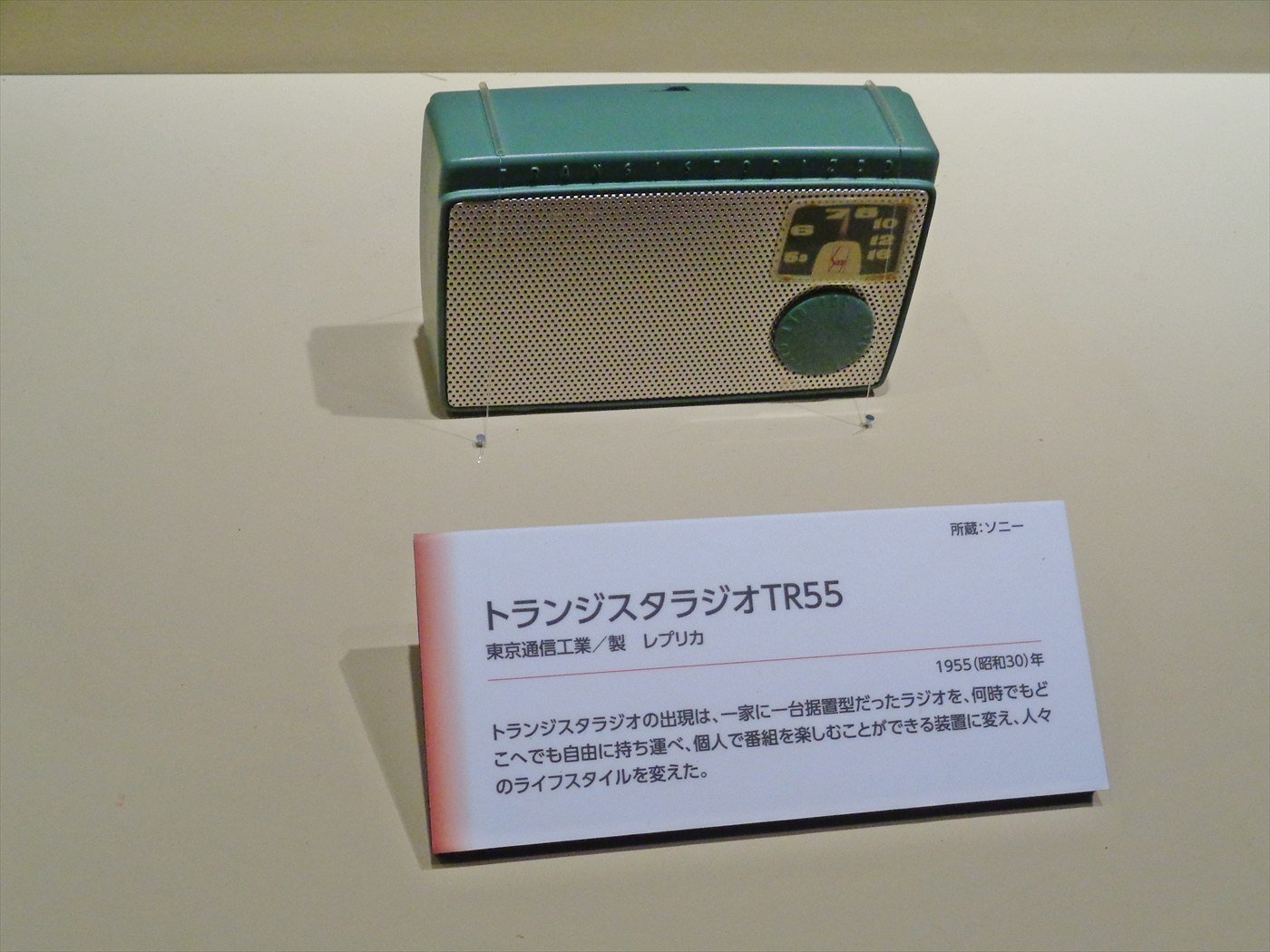 Sony’s TR-55 transistor radio, a small green-and-cream set, in a museum display case above a Japanese information label.