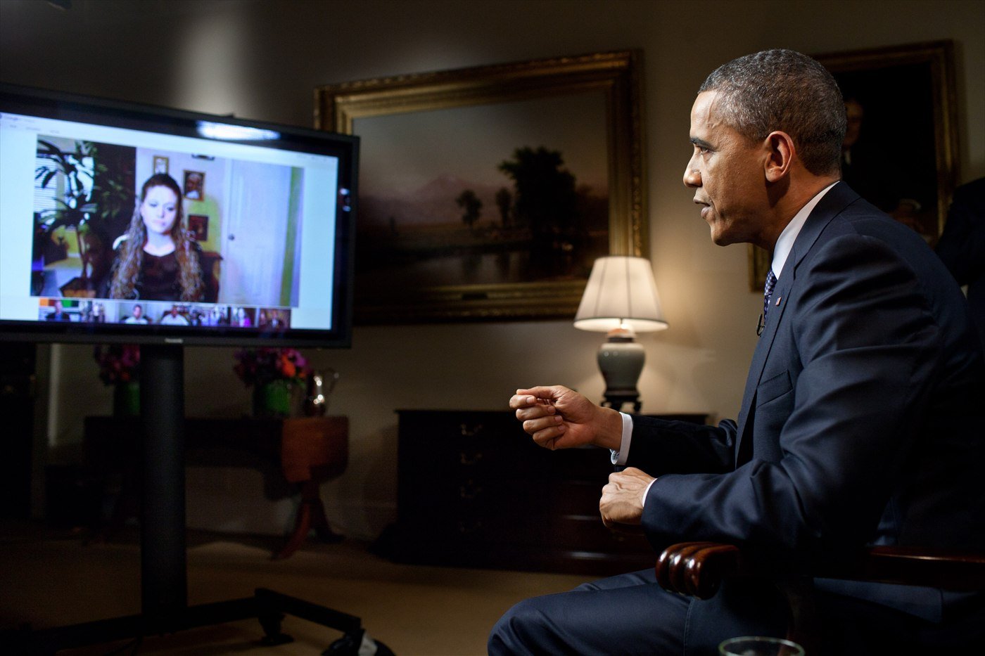 President Barack Obama seated in the Roosevelt Room of the White House, answering a question from a questioner shown on a video screen, during a YouTube interview in 2012.