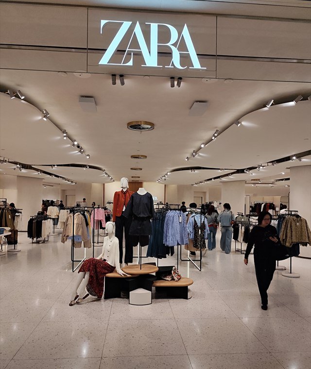 The inside of a Zara store in Hong Kong’s IFC Mall, with the Zara sign above rails of clothing and shoppers walking through.
